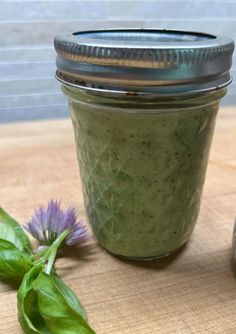 a jar filled with green liquid sitting on top of a wooden table next to a purple flower