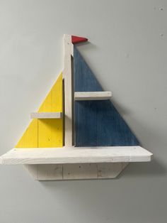 a wooden shelf with a blue and yellow sail on it's top, against a gray wall