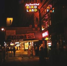 people are walking down the street at night in front of some buildings with neon signs