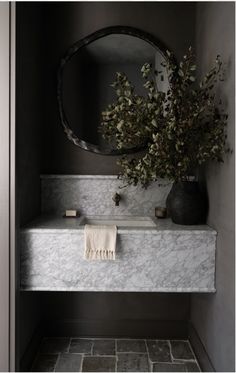 a bathroom with marble counter tops and a round mirror on the wall, along with a vase filled with flowers