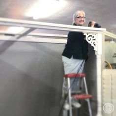 an older woman standing on top of a step ladder next to a white table and chair