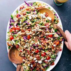 a large salad on a white plate with wooden spoons