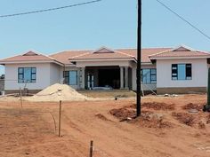 a house under construction in the middle of a dirt field with power lines above it