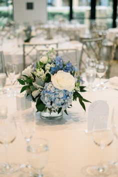 a vase filled with blue and white flowers sitting on top of a table covered in wine glasses