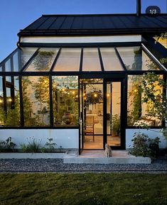 a house that is lit up at night with lights on the windows and plants growing outside