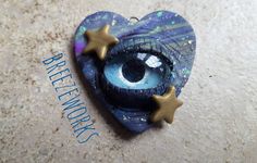 a heart shaped brooch with an eye in the center and stars hanging from it