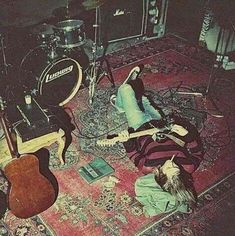 a man laying on the floor with his guitar in front of him and other instruments behind him