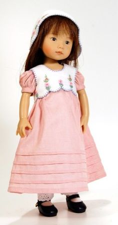 a doll wearing a pink dress and bonnet with flowers on her head, standing in front of a white background