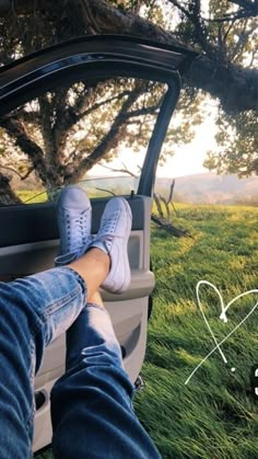 someone's feet sticking out the window of a car in front of a tree