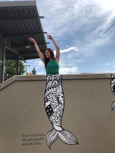 a woman standing on top of a cement wall next to a fish painted on it