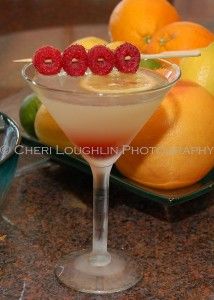 a martini with raspberries in it on a plate next to lemons and oranges