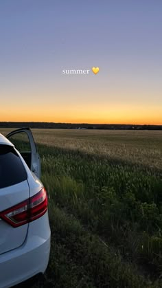 the back end of a white car parked on top of a grass covered field at sunset