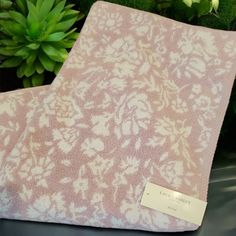 a pink and white blanket sitting on top of a table next to a potted plant