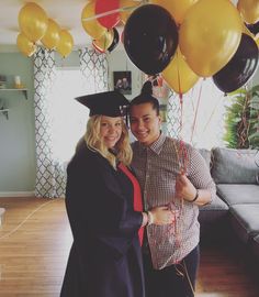 a man and woman in graduation gowns posing for a photo with balloons on the ceiling