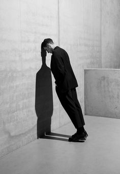 a man in a suit leaning against a wall with his hand on his head and looking down