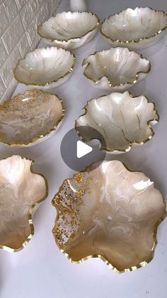 six white and gold leaf shaped dishes sitting on a table next to a brick wall