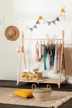 a rack with clothes hanging on it next to a basket and hat holder in front of a wall