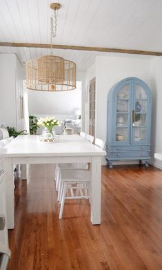 a white table and chairs in a room with wood floors, cabinets and a blue hutch