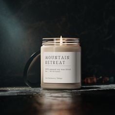 a lit candle sitting on top of a wooden table next to a black mug with the words mountain retreat written on it