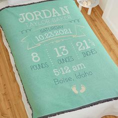 a baby's birth announcement blanket sitting on top of a bed next to a night stand