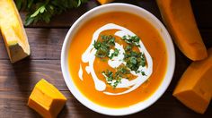 a bowl of carrot soup with sour cream and parsley in the center on a wooden table