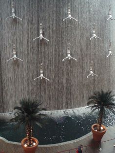 people are standing in front of a fountain with water falling from it and palm trees on either side