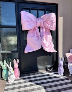 a pink bow on the front door of a house with stuffed animals around it and an easter bunny figurine next to it