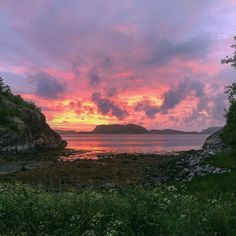 the sun is setting over an island in the middle of the ocean with rocks and grass on both sides