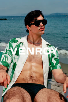 a man sitting on top of a beach next to the ocean wearing sunglasses and a green shirt