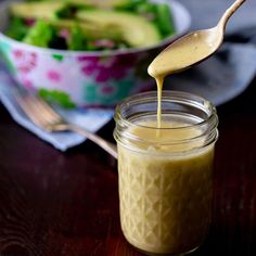 a spoon full of dressing being poured into a jar with salad in the back ground