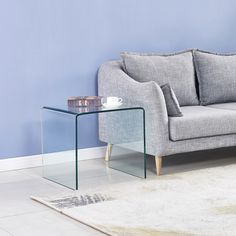 a grey couch sitting next to a glass table on top of a white carpeted floor