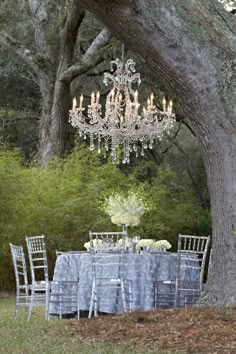 an outdoor table set up under a tree with chandelier