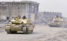 two tanks are parked in front of a building and another tank is on the road