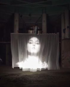 a woman's face is projected through curtains in the middle of a dark room