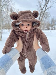 a baby in a bear costume being held up by someone's hands and wearing mittens