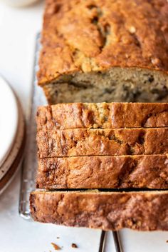 a loaf of banana bread sitting on top of a metal rack next to a plate