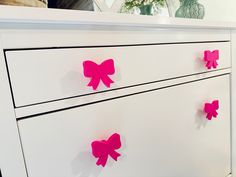 a white dresser with pink bows on the drawers and mirror in the backgroud