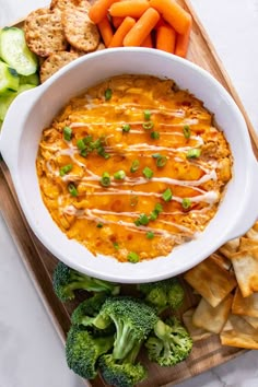 a white bowl filled with dip surrounded by veggies and crackers on a cutting board