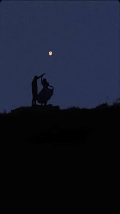 two people standing on top of a hill under a full moon at night, silhouetted against a dark blue sky