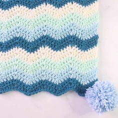 a crocheted blue and white blanket with a pom - pom on it