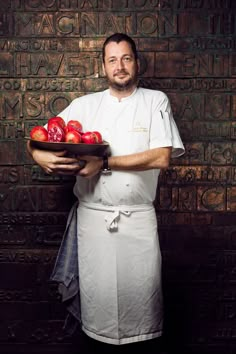 a man in an apron is holding a tray of apples and oranges on his left hand