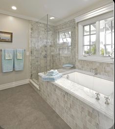 a bath room with a tub a sink and two towels hanging on the wall in front of a window