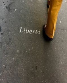 a person in yellow pants and brown shoes standing on the sidewalk with their feet up