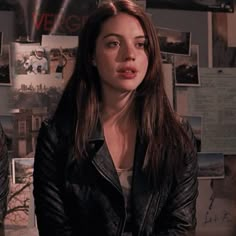 a woman sitting in front of a wall with pictures on the walls and posters behind her