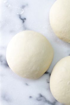 three uncooked doughnuts sitting on a marble counter top next to each other