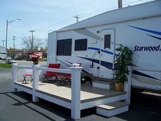 a camper parked in a parking lot next to a red chair and potted plant