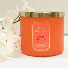 peach bellini scented candle with white flowers in the background and a gold rimmed lid