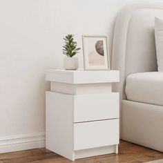 a white nightstand next to a bed with pillows and a plant on top of it