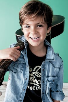 a young boy is smiling and holding a guitar in his hand while wearing a denim shirt