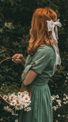 a woman in a green dress is holding daisies